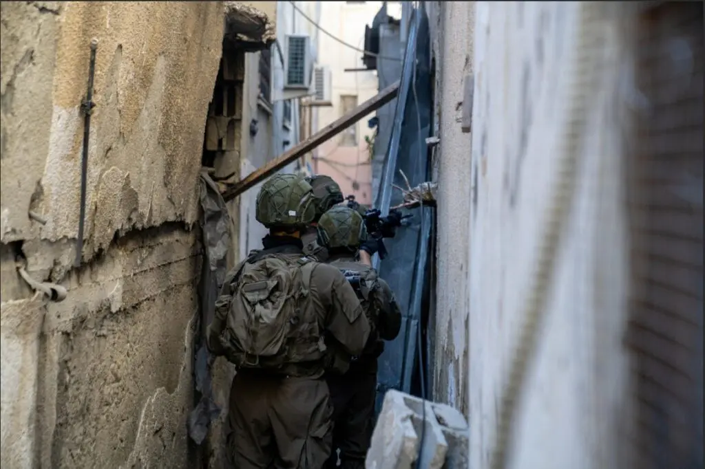 Soldiers navigating narrow alleyway in urban area.