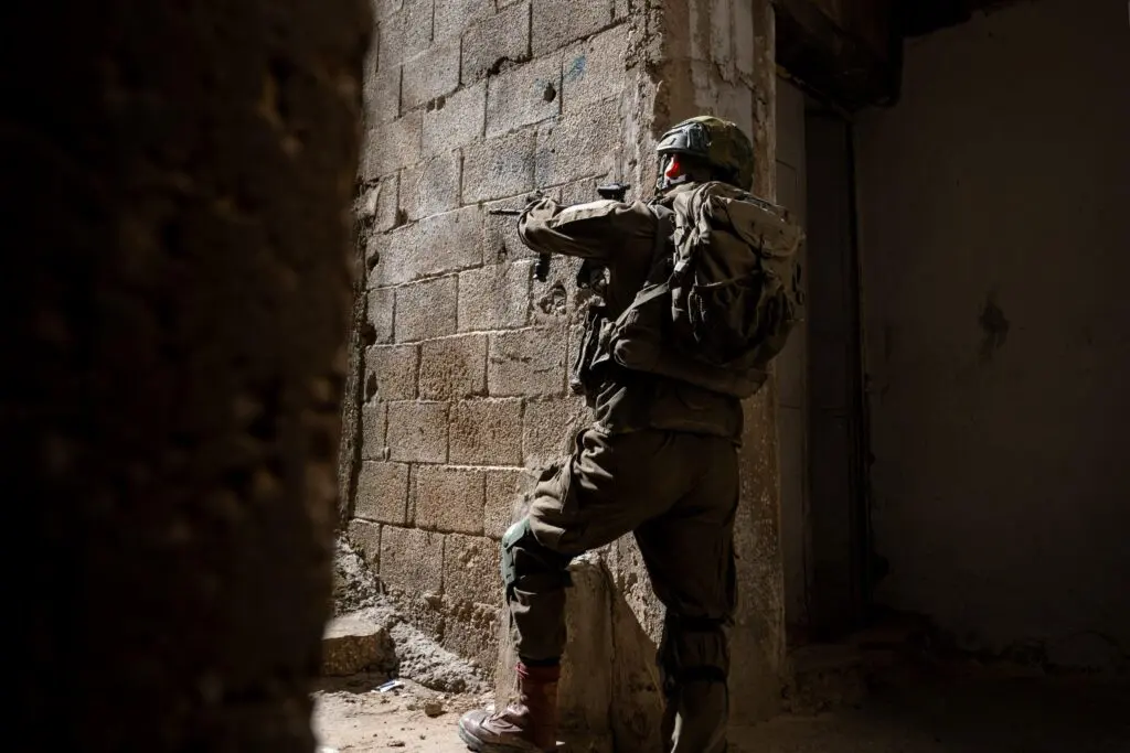 Soldier in tactical gear aiming weapon in alleyway.