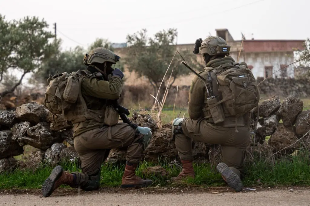 Two soldiers kneeling, observing rural area.