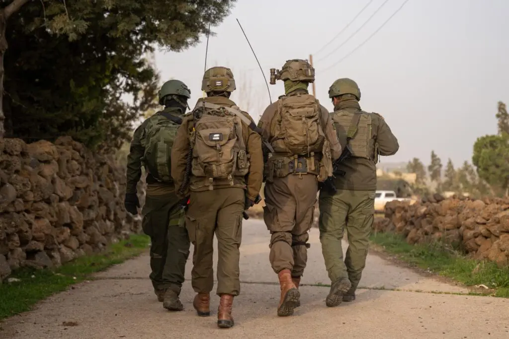 Four soldiers walking down rural path, backs facing camera.