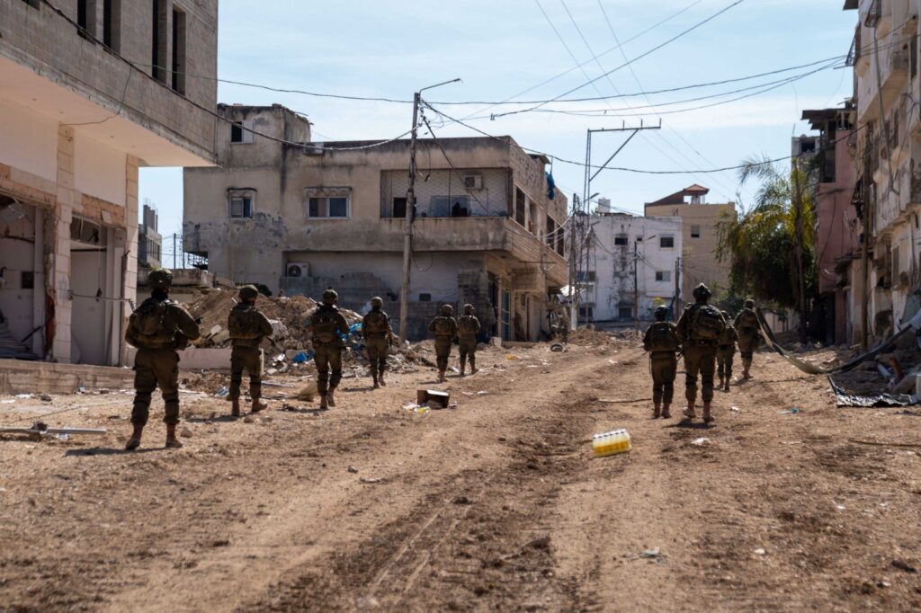 Soldiers patrol a damaged urban area.