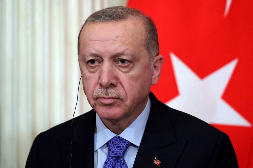 Person in suit with headphones in front of flag.
