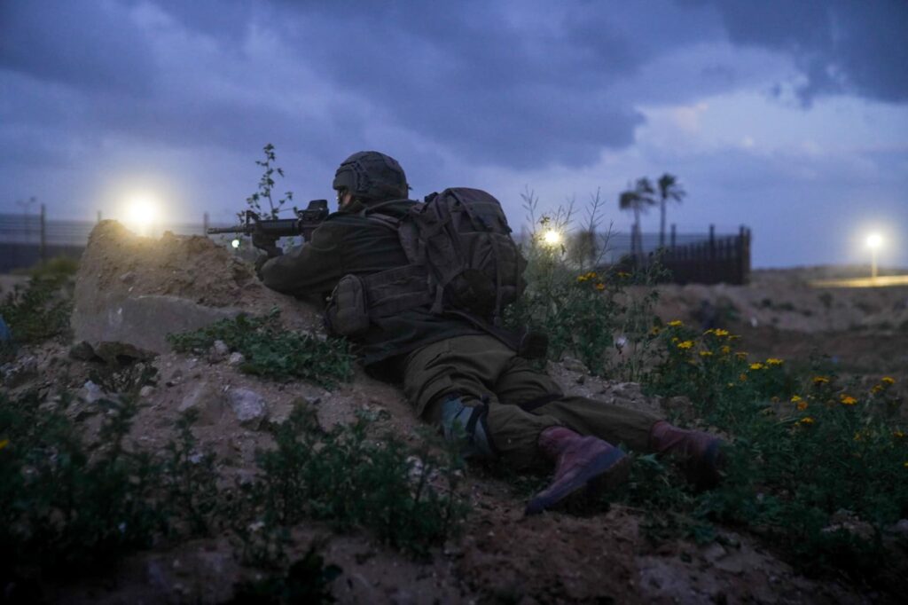 Soldier aiming rifle in nighttime field operation.