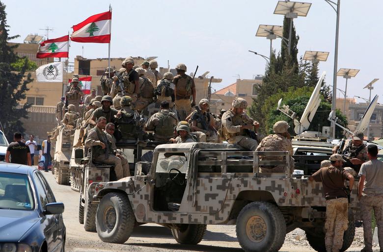 Military convoy with Lebanese flags on city street.