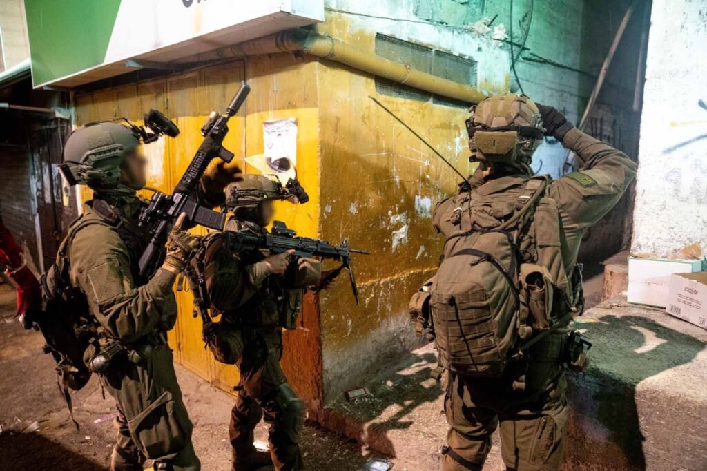 Soldiers with rifles on street patrol at night.