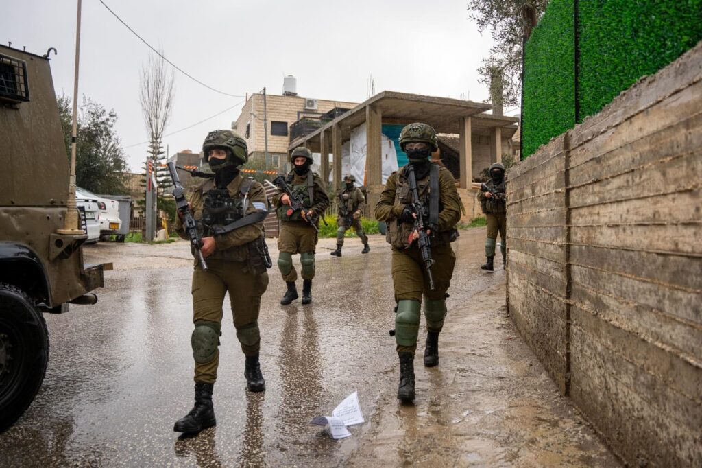 Soldiers patrolling a wet street in military gear.