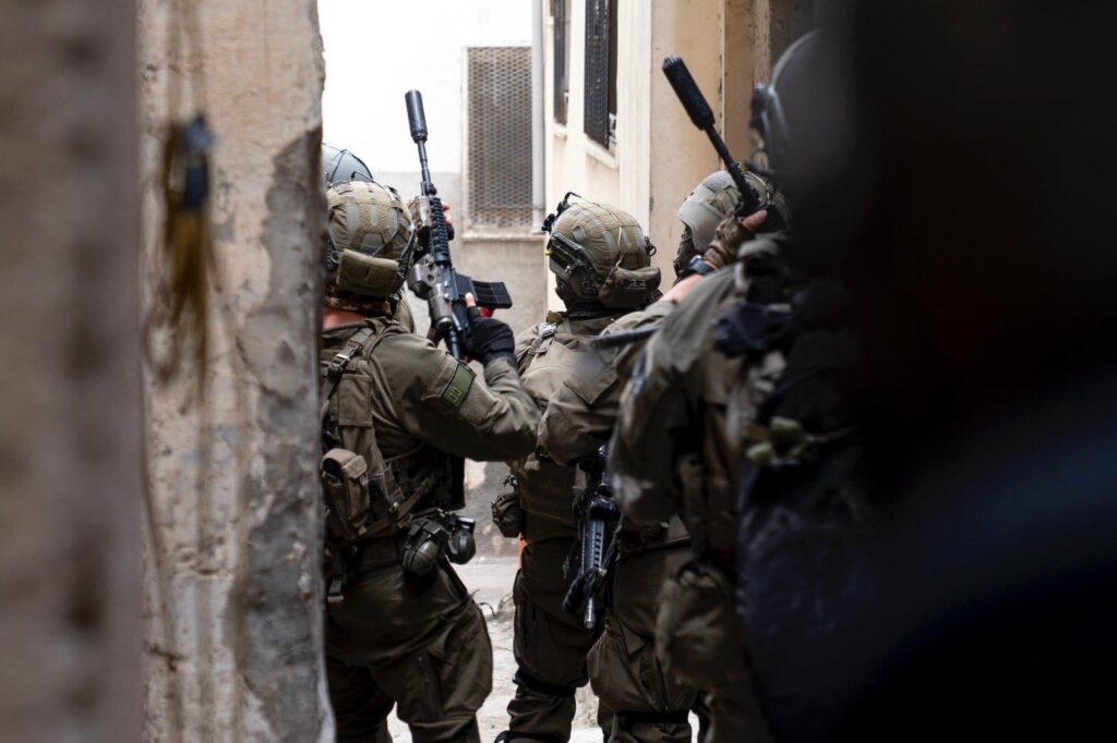 Soldiers in tactical gear moving through alley.