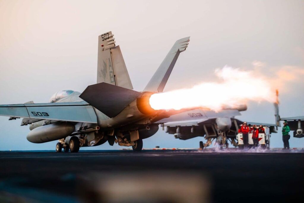 Fighter jet taking off from aircraft carrier deck.